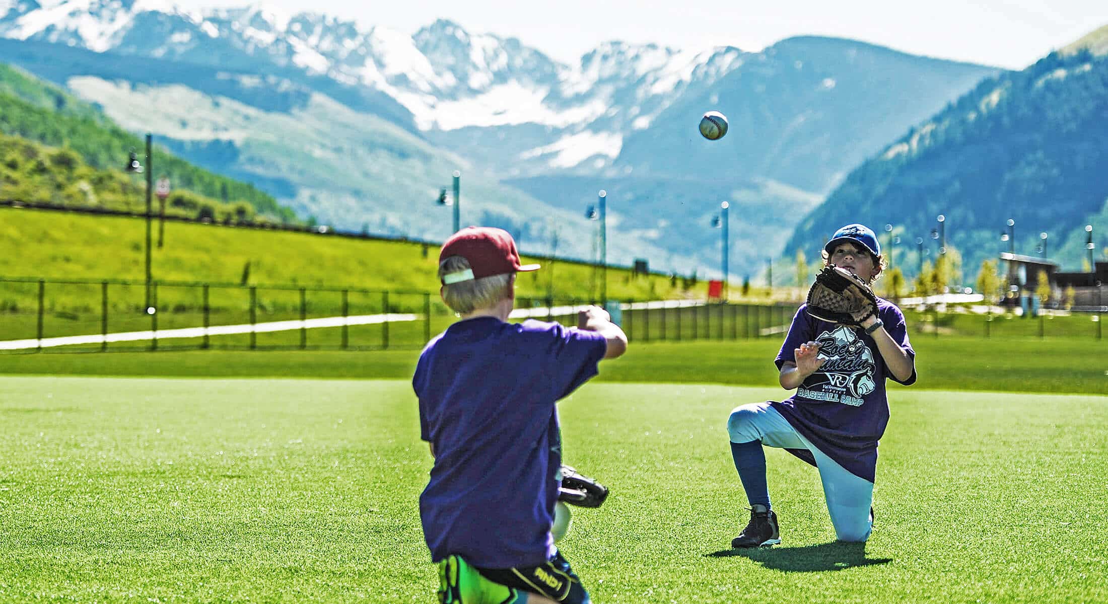 Two boys playing baseball in a field with mountains in the background in Vail.