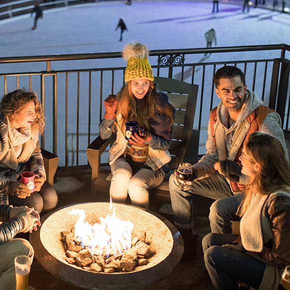A group of people sitting around a fire pit at night while fishing.