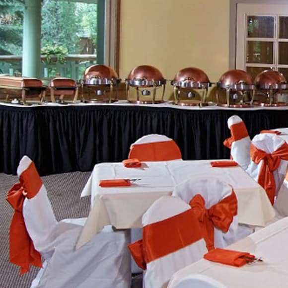A banquet room set up with orange and white tablecloths.