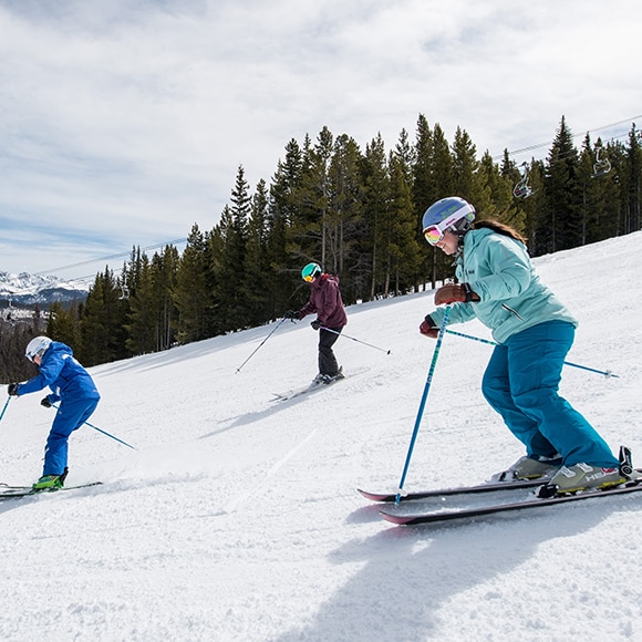 A group of people skiing down a snowy slope in Vail.