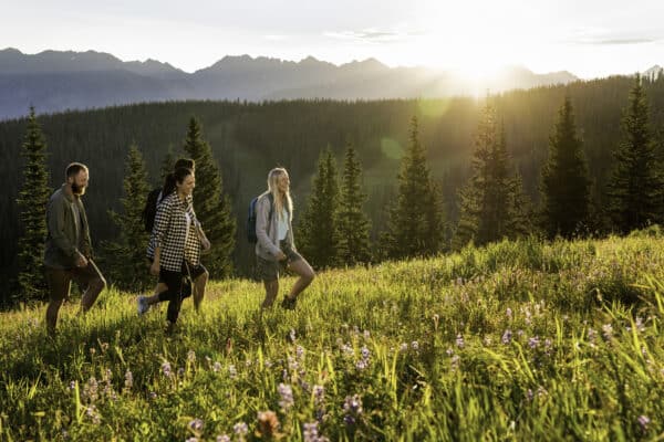 Three women walking in a grassy meadow with mountains in the background in Vail, Colorado.
