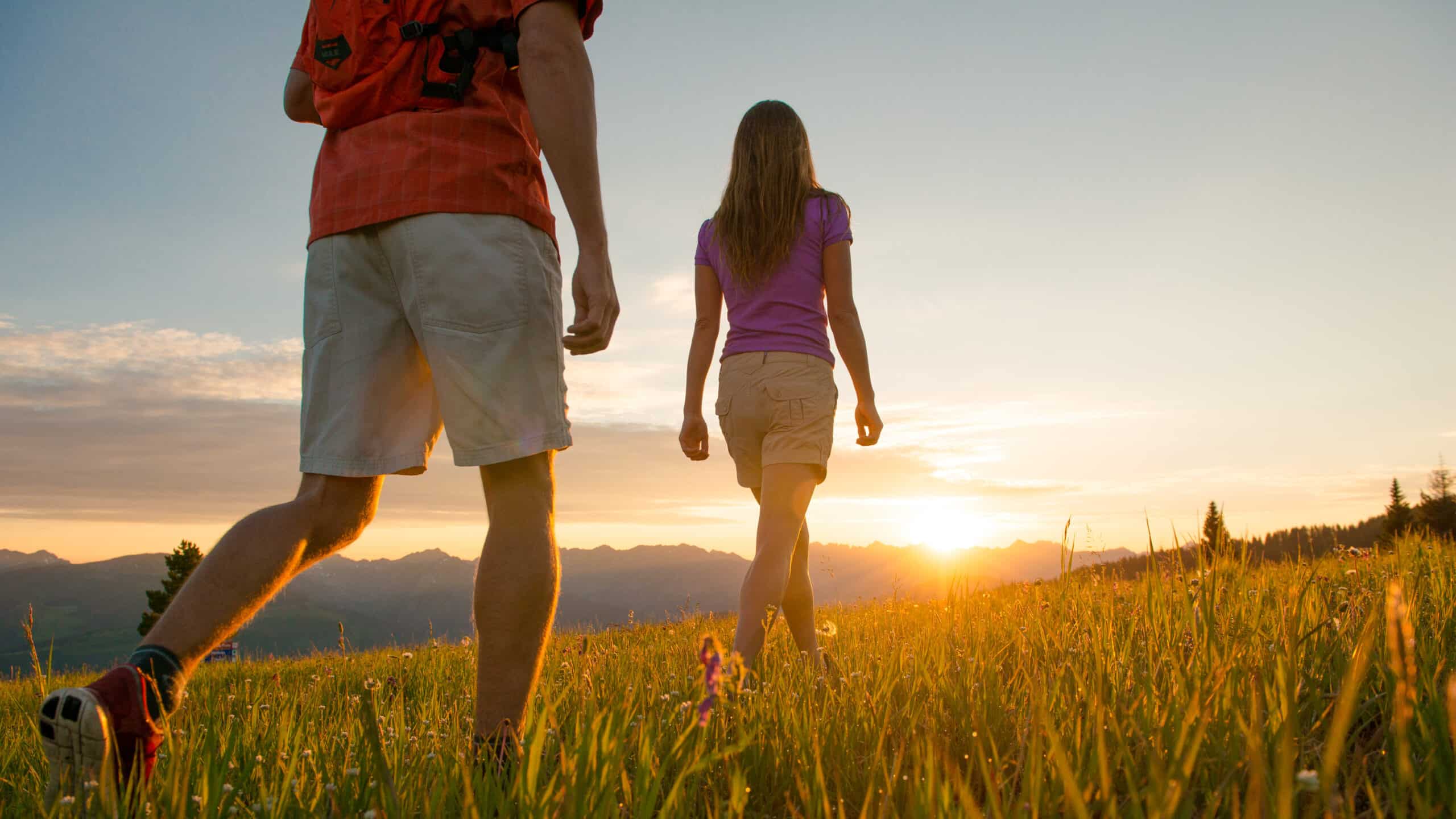 Two people walking on a grassy field at sunset.