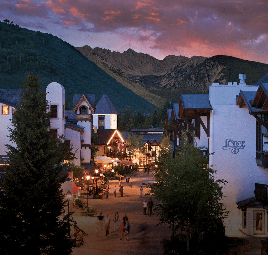 A mountain village at dusk with people walking down the street.