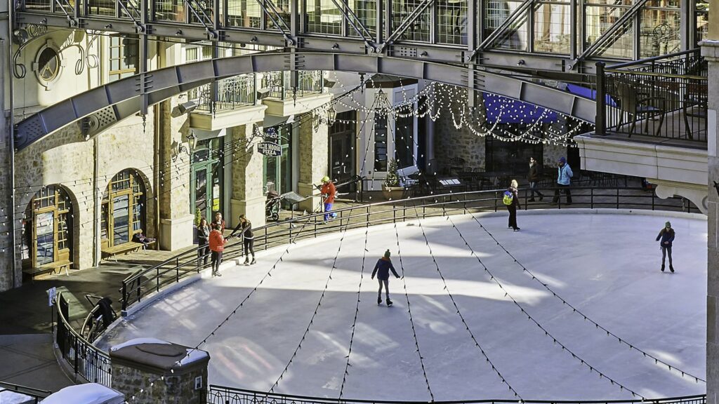 Ice skaters glide on the Alderhof Ice Rink at The Arrabelle at Vail Square in Lionshead Village in Vail. Glittering lights are strung above the rink.