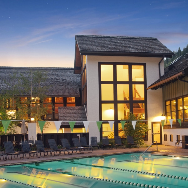 Vail Racquet Club Pool at dusk with building in the background and white and green flag hanging over the pool
