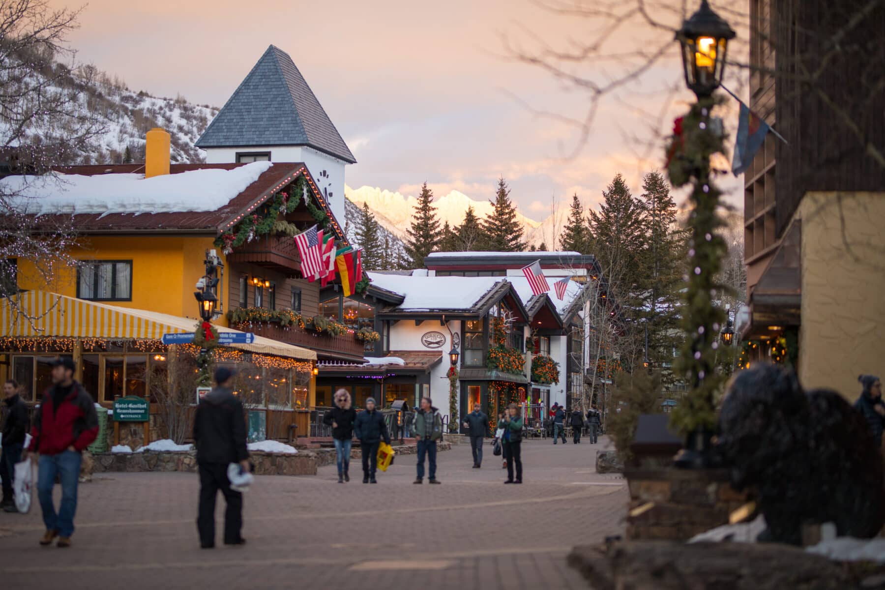 A street in Vail, Colorado, is festooned with holiday greenery. People dressed in warm clothing meander the street with their shopping bags in hand.