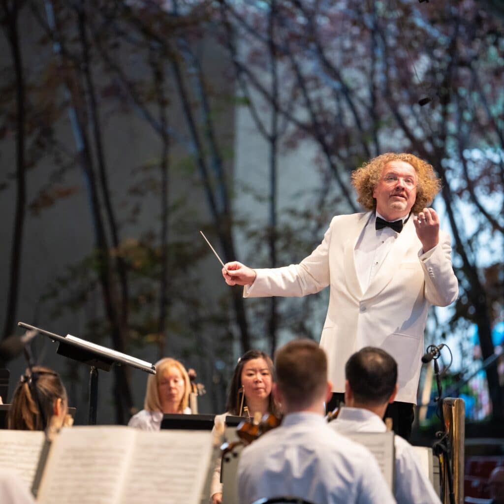 A man in a white tuxedo conducting an orchestra.