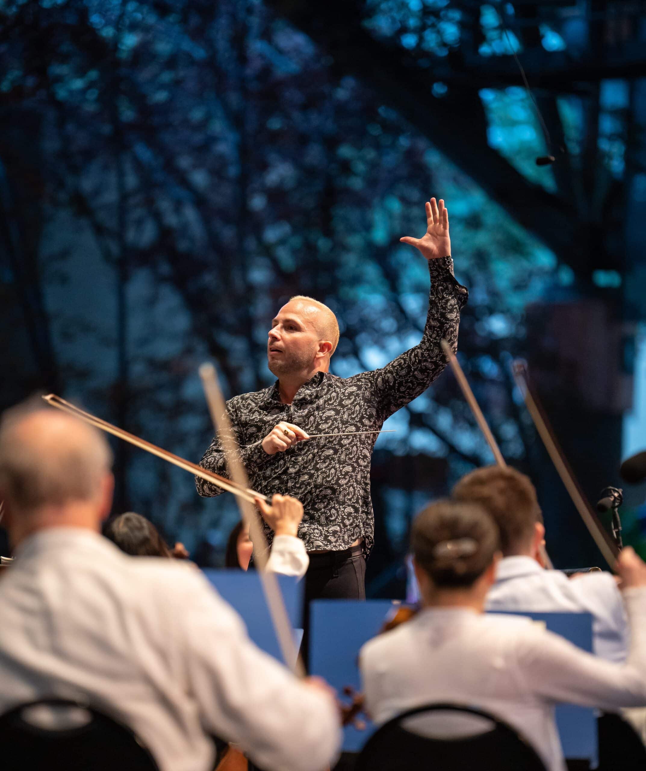 A conductor is conducting an orchestra in front of an audience.