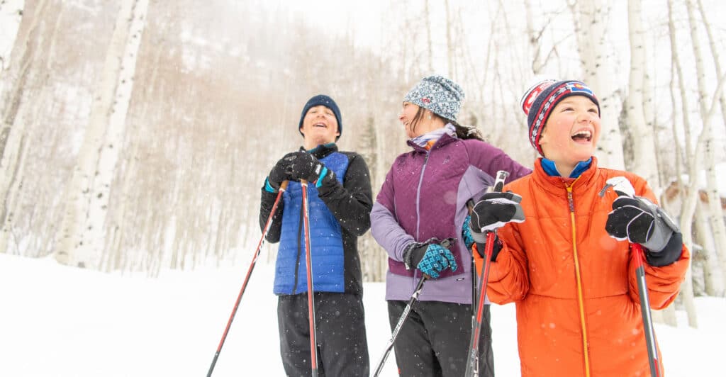 A family of three cross-country skis in a snowy glade in Vail, Colorado.
