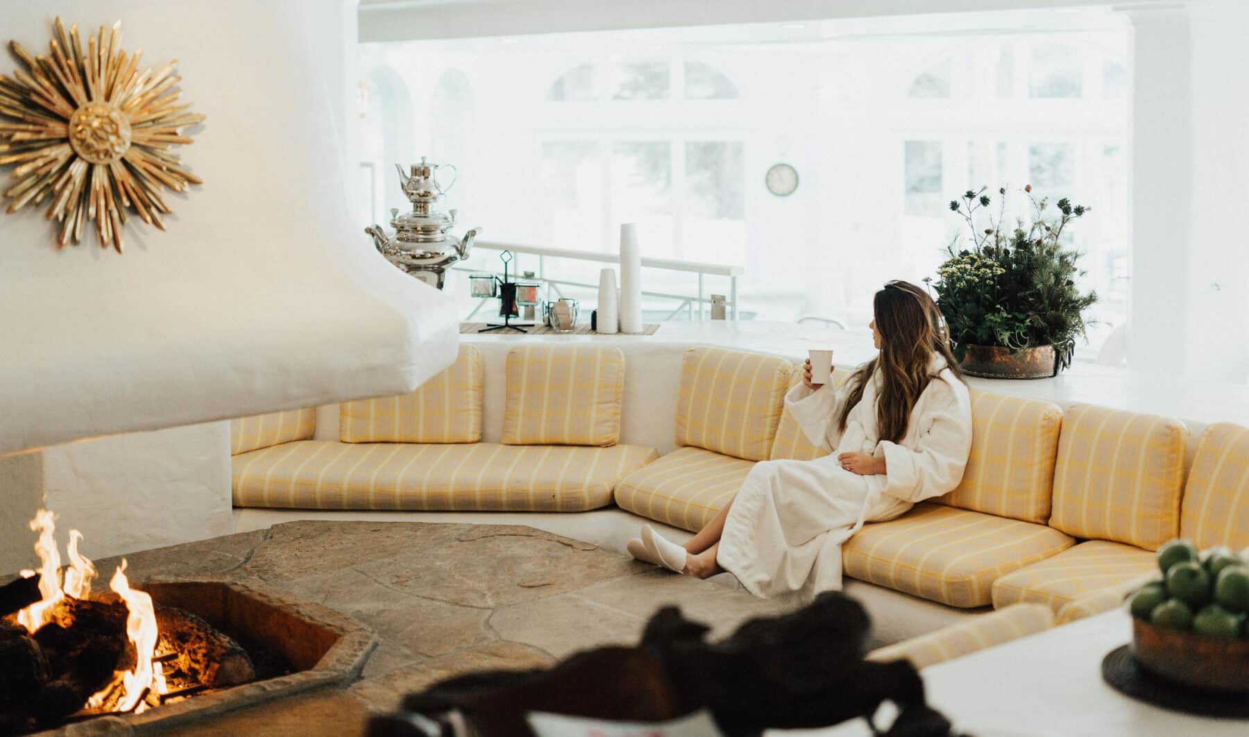 Woman enjoys a warm drink while siting next to a fit place at the Sonnenalp Spa in Vail