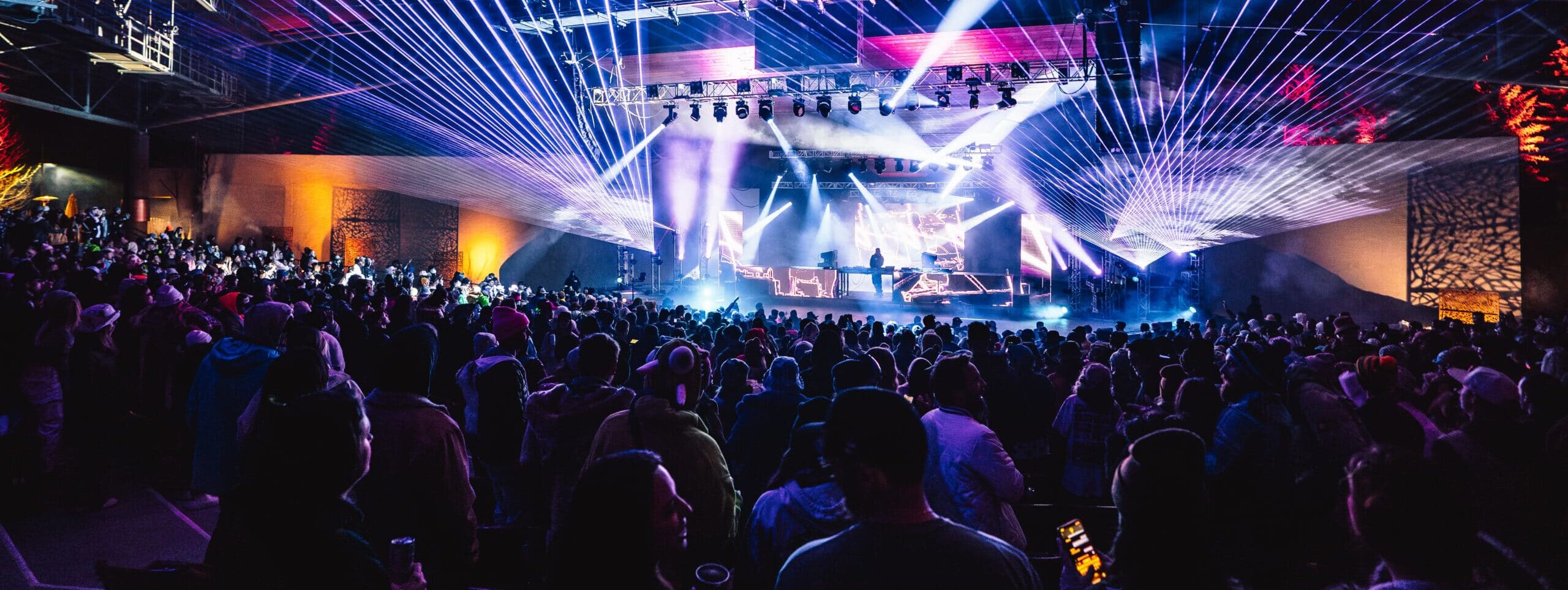Colorful lights and smoke illuminate the ceiling of the Gerald R. Ford Amphitheater while two drummers stand on stand before a large ground.