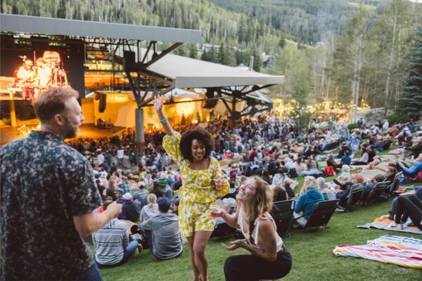 A person in a yellow, patterned romper dances and waves a hand in the air during a packed concert at The Amp in Vail Village.