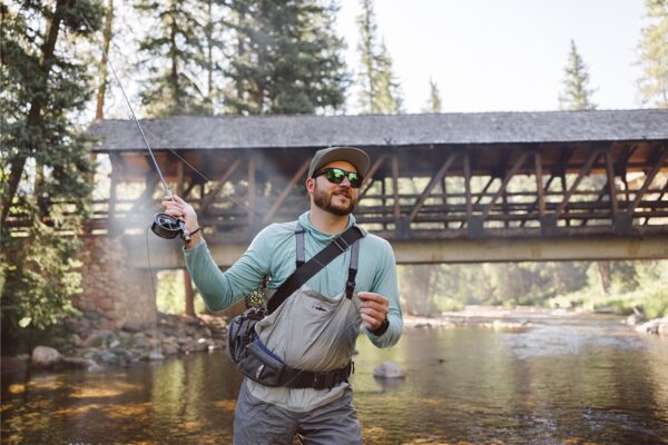 A person in a light-teal, long-sleeve shirt and fishing gear swings back their arm to cast a line on the Gore Creek near Vail Village in Colorado.