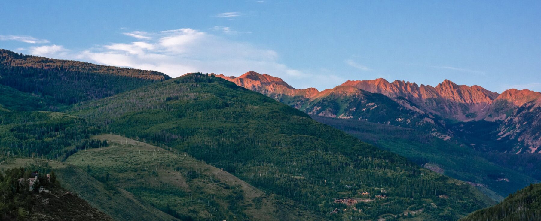 The mountain peaks near Vail Village, Colorado, glow a pink-purple color from the rays of the sun sinking below the horizon out of view.