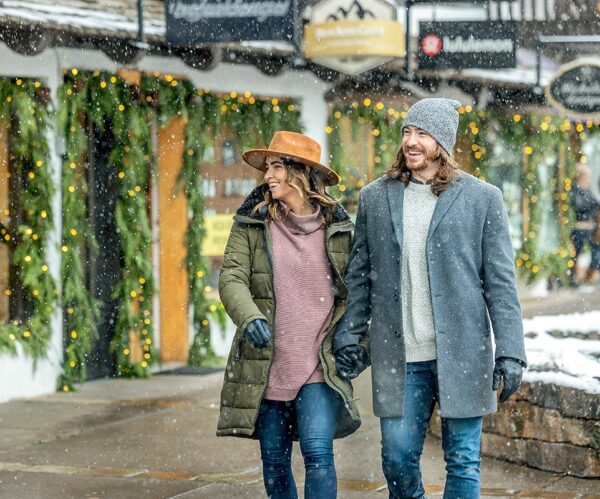 A couple walks arm in arm along the snowy streets of Vail, Colorado, looks at different store fronts.
