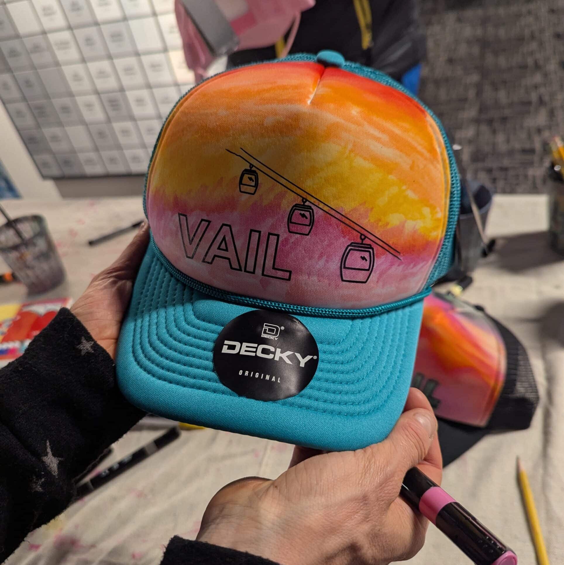 Blue trucker hat decorated with VAIL and bright colored markers