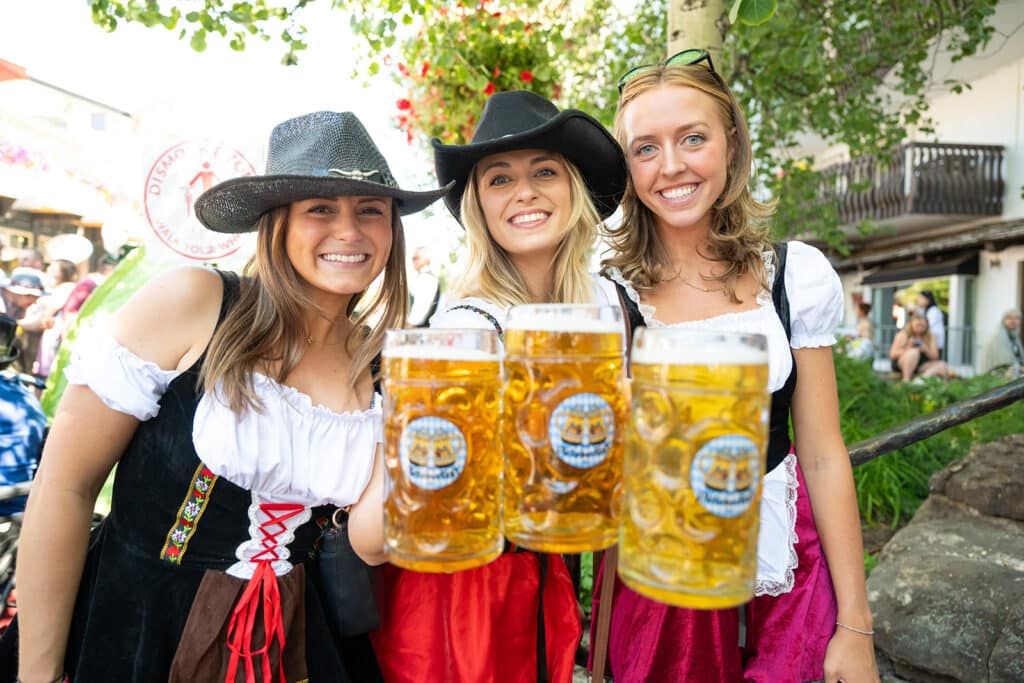 three girls wearing dirndls holding Oktoberfest steins