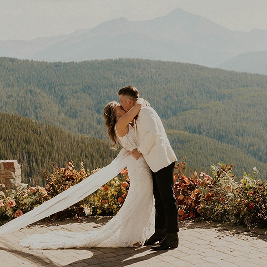 A bride and groom share a loving kiss at their wedding ceremony near Vail, Colorado, with the Rocky Mountains in the background.