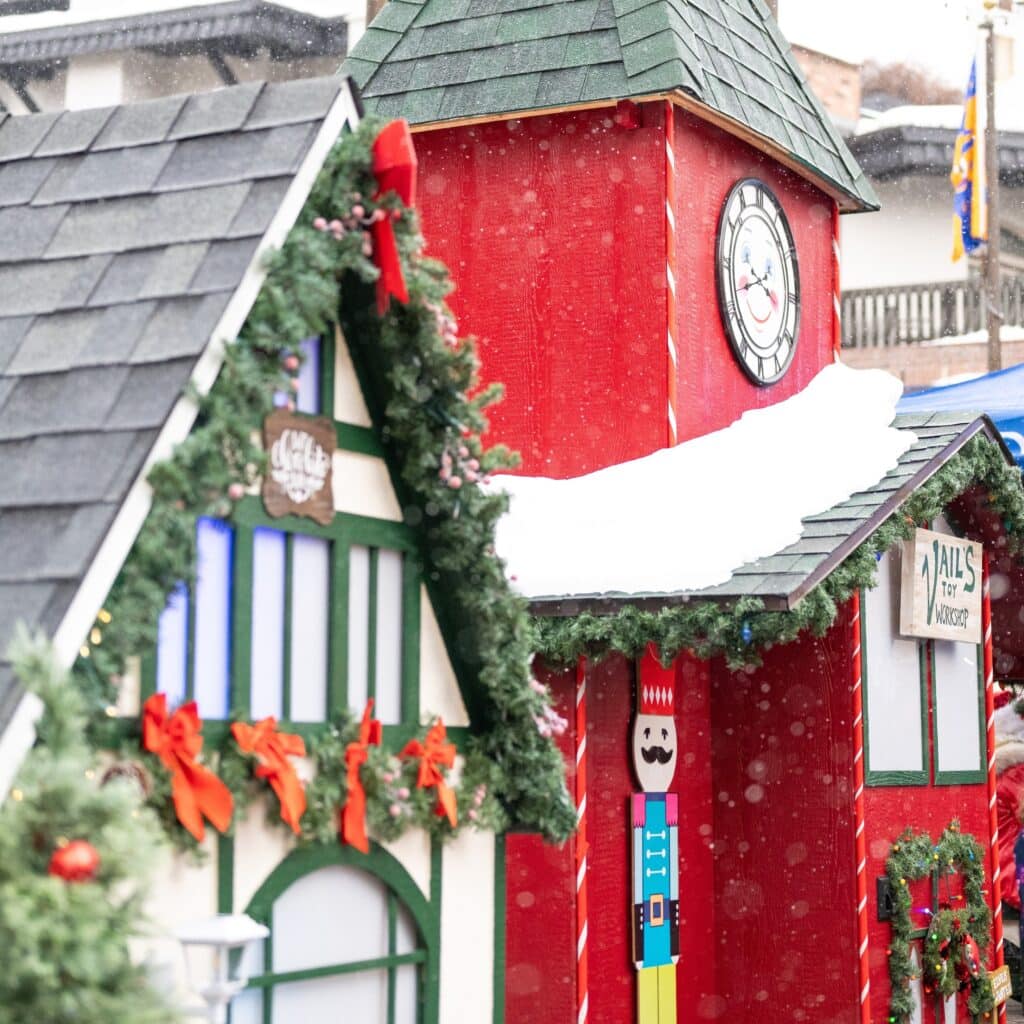 A festive outdoor scene with snow, red and green holiday decorations, a clock tower, garlands, and a toy soldier figure.