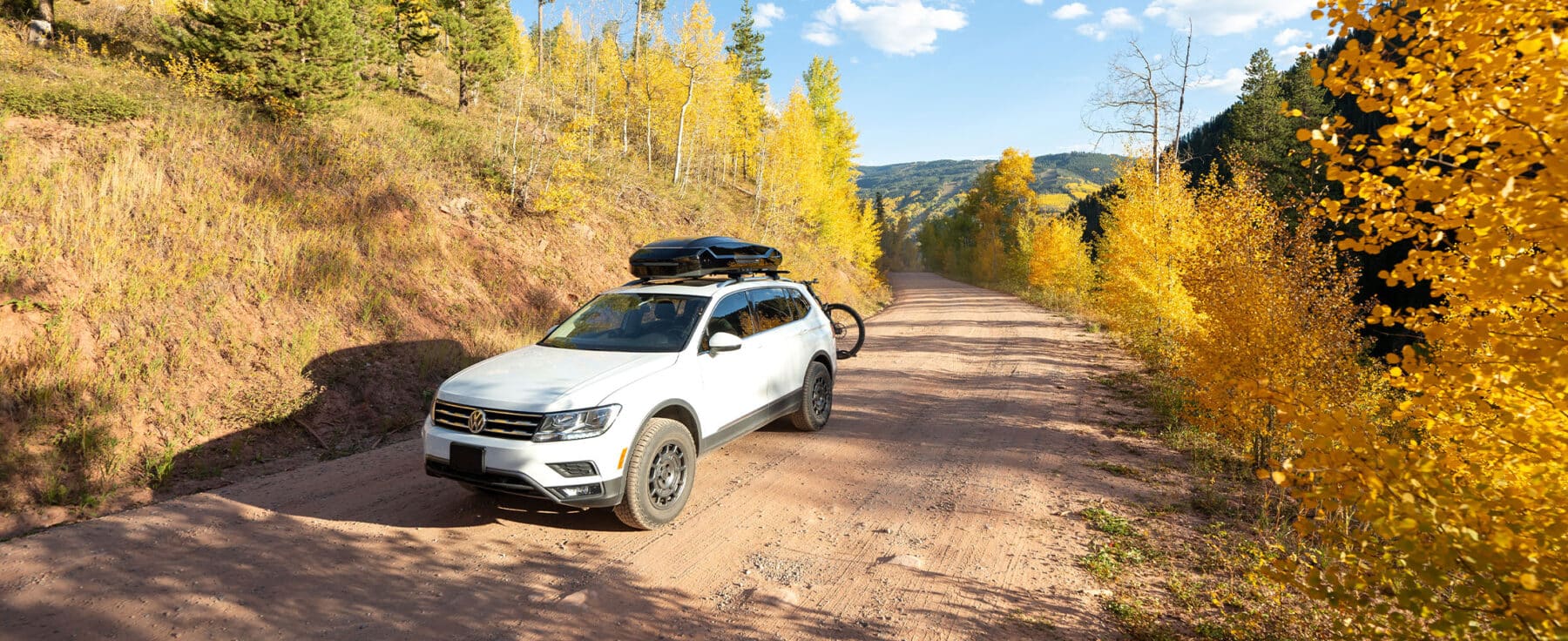 A white car drive through a narrow pass on a dirt road near Vail, Colorado, surrounded by golden fall foliage.
