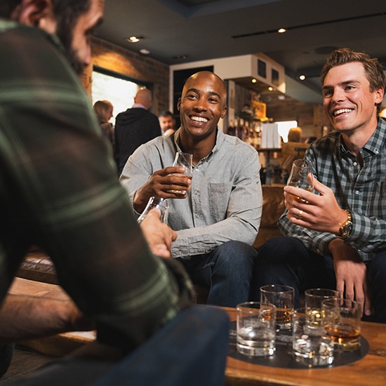 Three men sip glasses of amber liquid at 10th Mountain Whiskey & Spirits in Vail, Colorado.
