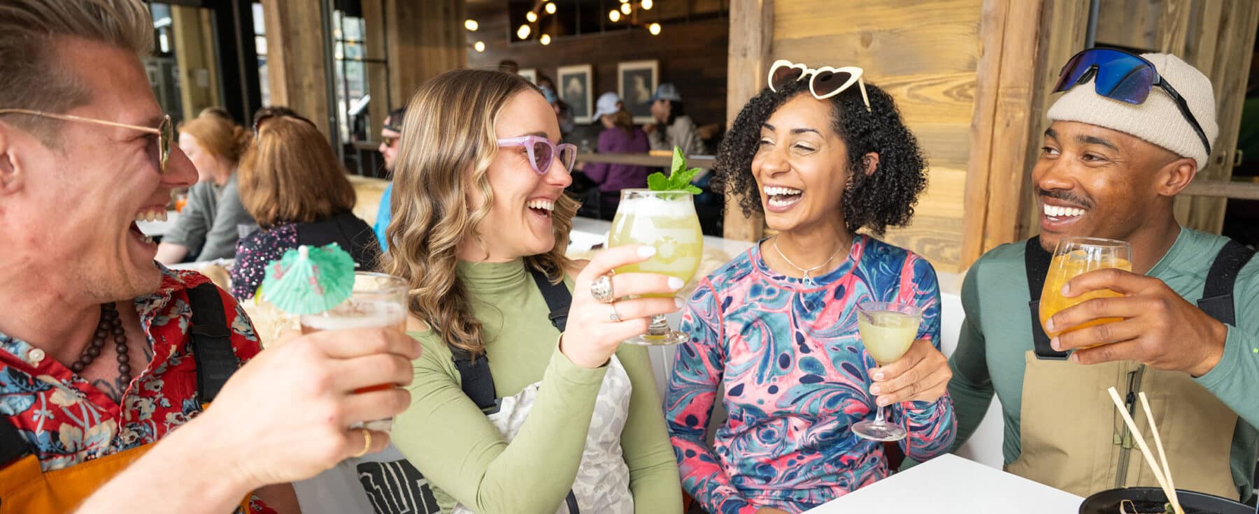 Four people are smiling and laughing as they raise their glasses around an outdoor table at Avanti F&B Vail in Vail, Colorado.