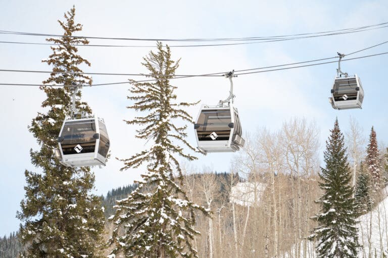 Three mountain gondola cars hang above snowy pine trees during winter.
