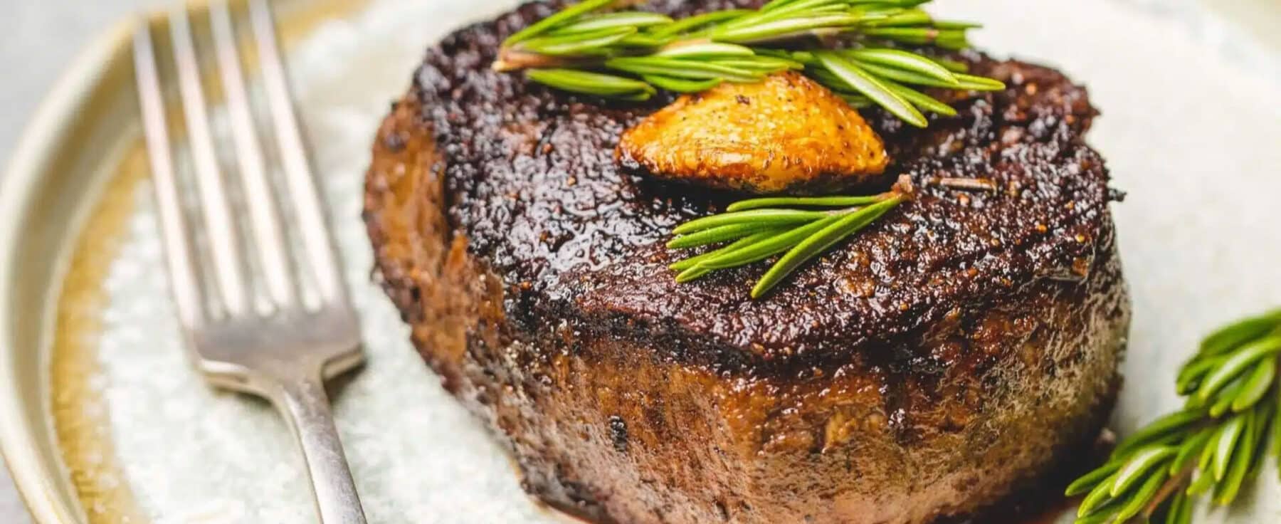 Close-up view of a steak on a plate topped with rosemary and garlic in Vail, Colorado.